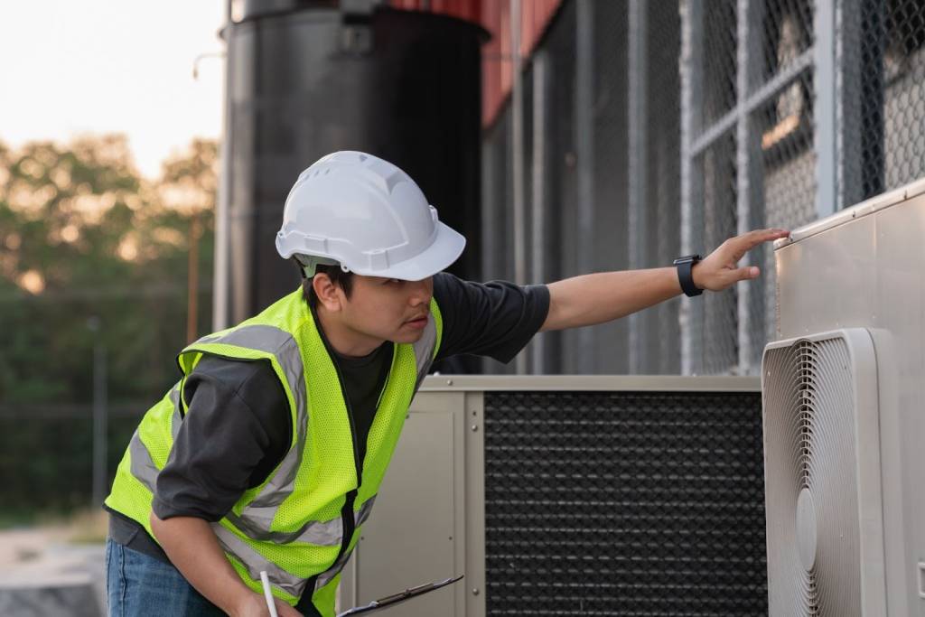 An HVAC service technician inspects an industrial air conditioning unit to inspect the cooling system performance.