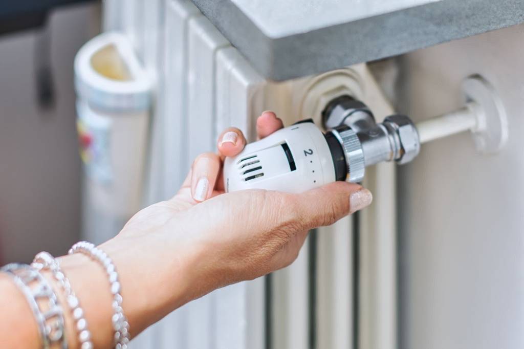 Close-up of a hand adjusting the control valve on a radiator. 
