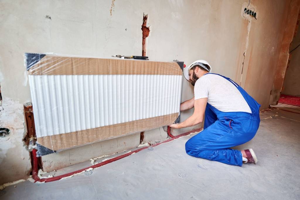 A HVAC technician installs a new radiator during a residential heating system upgrade in an apartment.