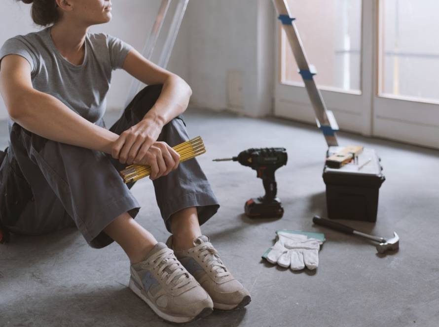 Woman with a measuring tool sits on the floor with renovation tools while contemplating the project