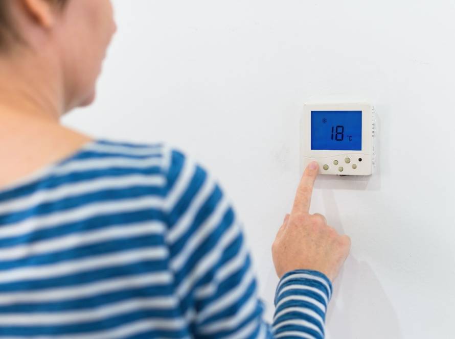 Rear view of a woman adjusting a home HVAC control unit