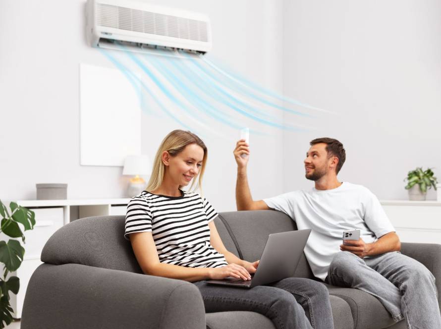 Couple on a sofa with the man controlling the AC by remote and cool air graphics blowing toward them while the woman works on her laptop