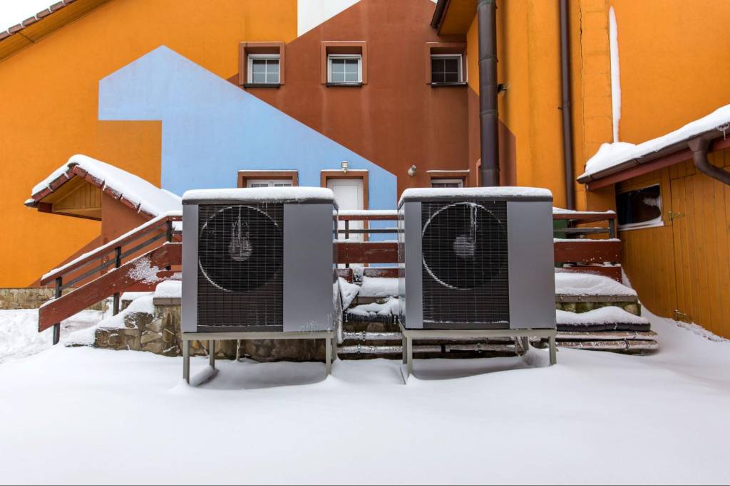 Two modern residential heat pump units installed behind an orange-colored house