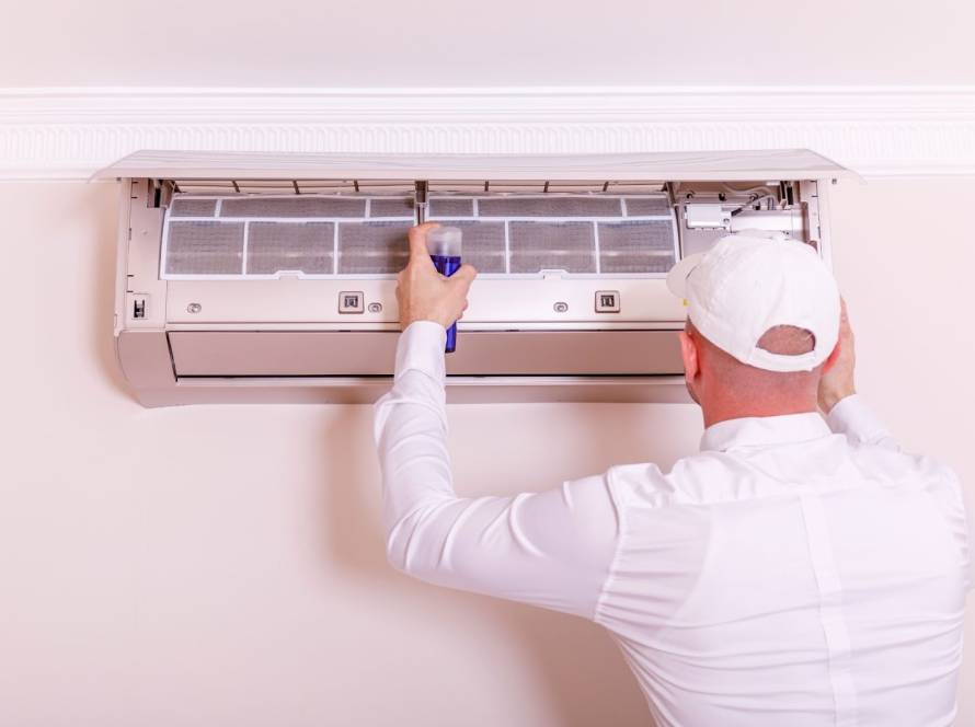 HVAC technician in a white uniform inspecting an indoor air conditioning system during routine maintenance