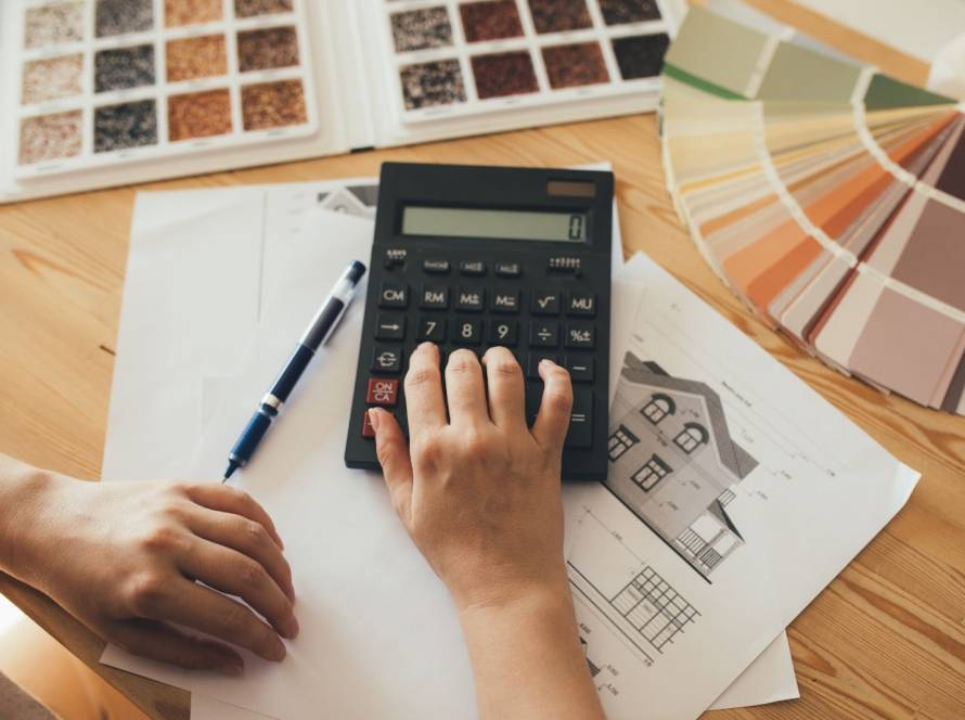 Overhead view of a woman calculating home renovation costs with a calculator and project plans