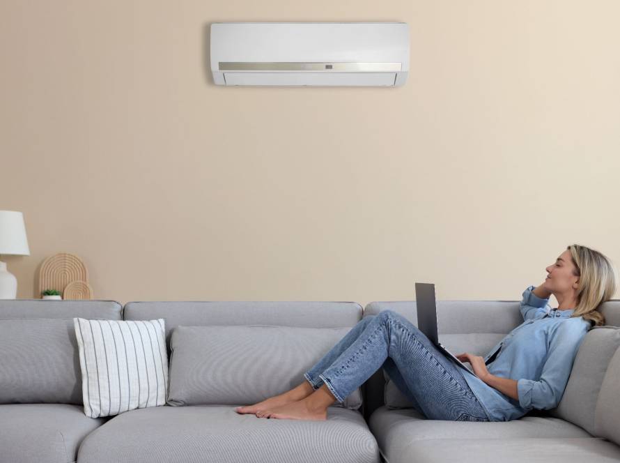 Woman relaxing on a sofa with a laptop under a wall-mounted ductless mini split air conditioner